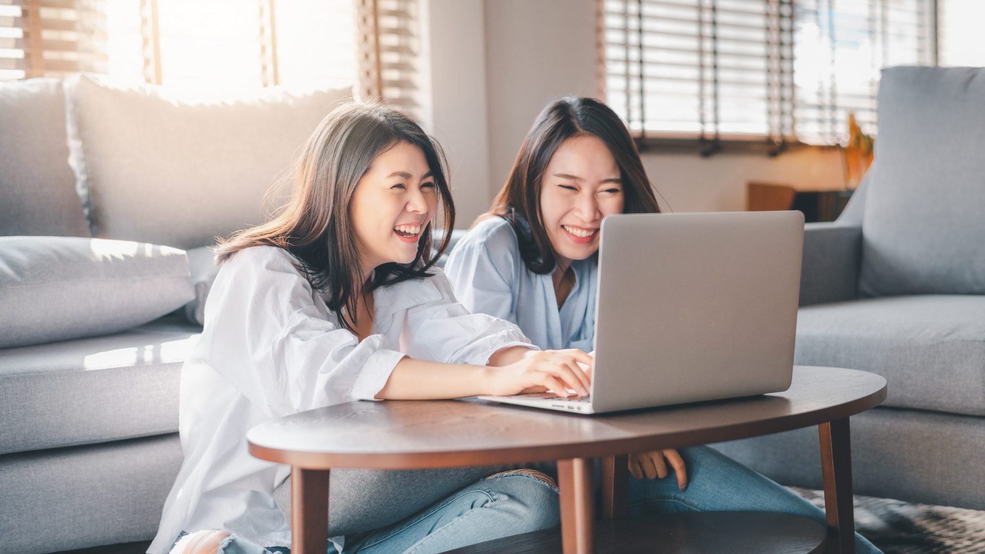 Two women happily working on a laptop in a cozy living room.