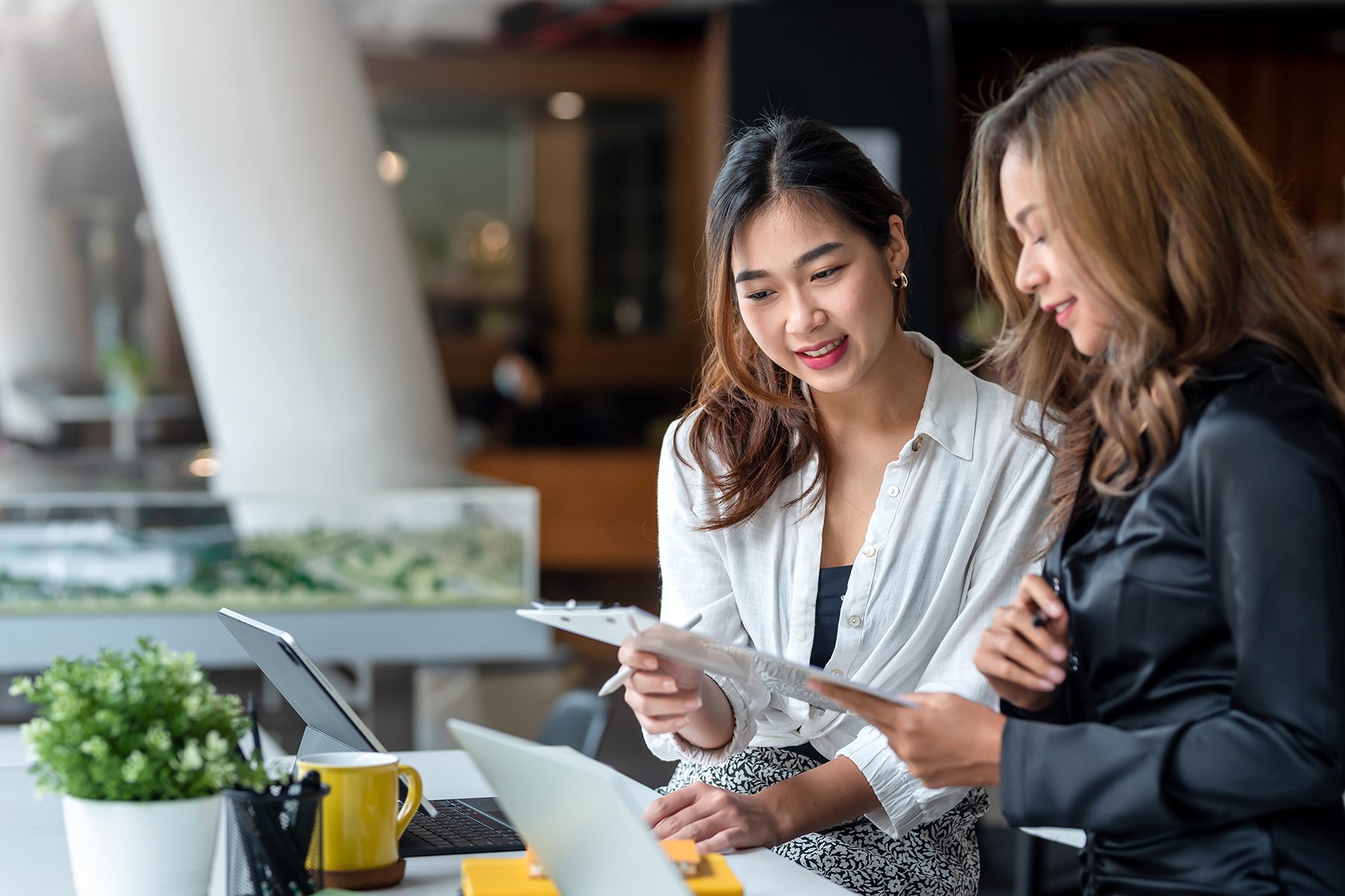 Two women discussing business plans in a modern office setting.