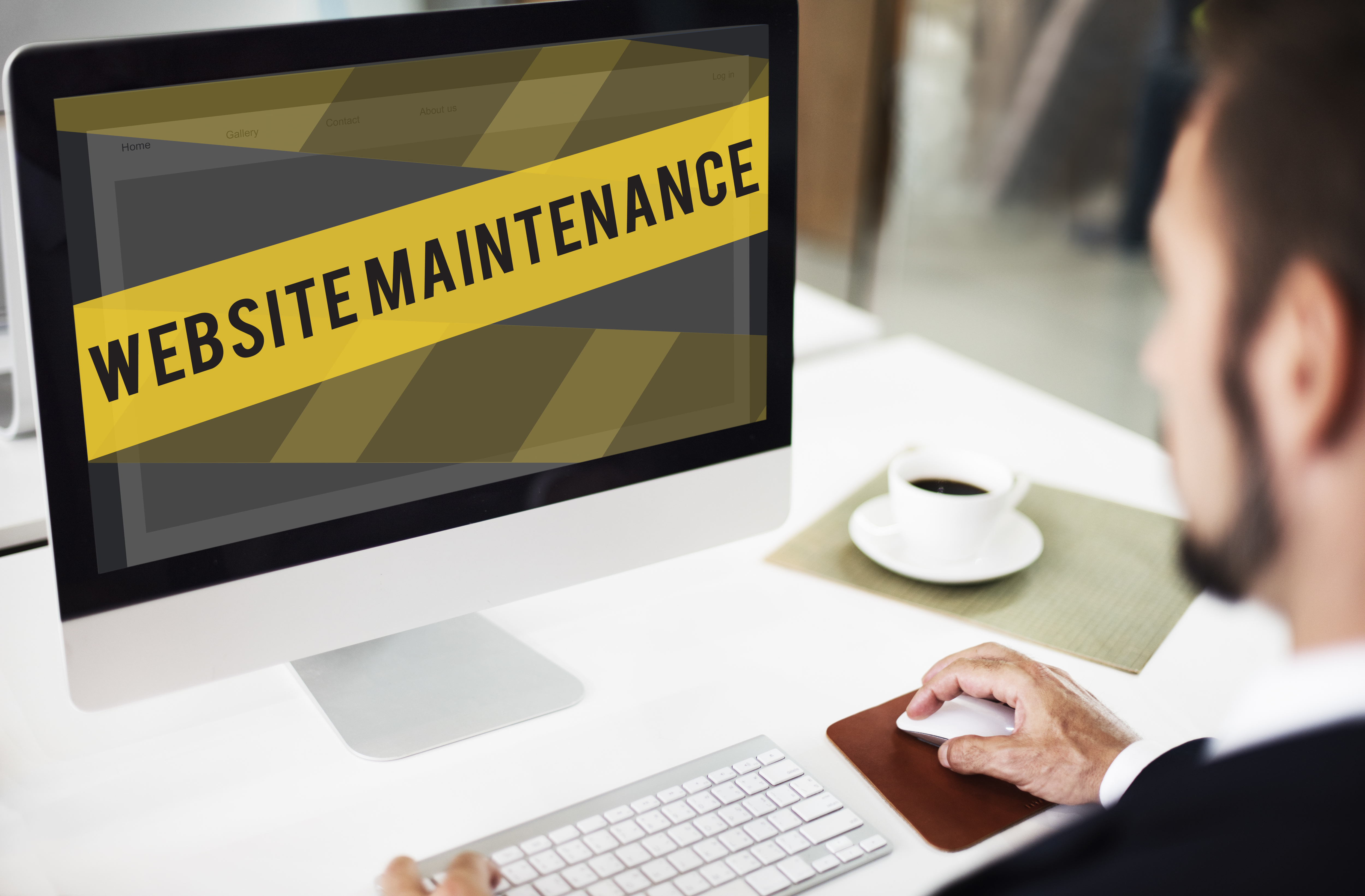 Man working on website maintenance at a desk with a computer and coffee.