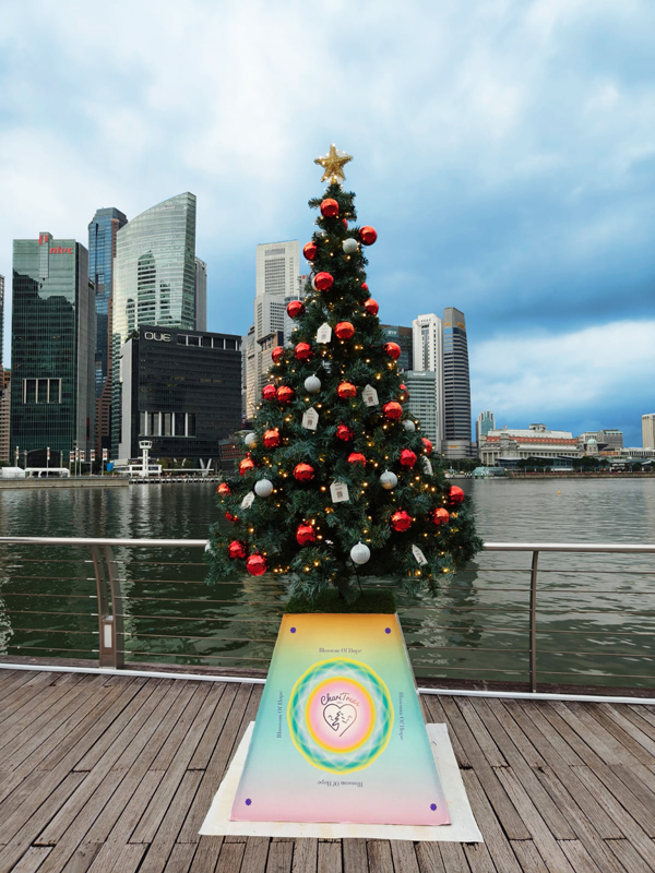 Christmas tree decorates Singapore waterfront with modern skyscrapers behind.